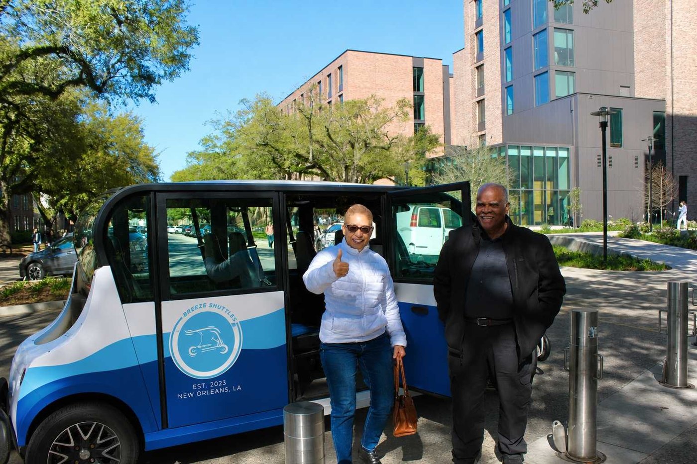 Riders giving a thumbs up beside a Breeze shuttle on a sunny campus street
